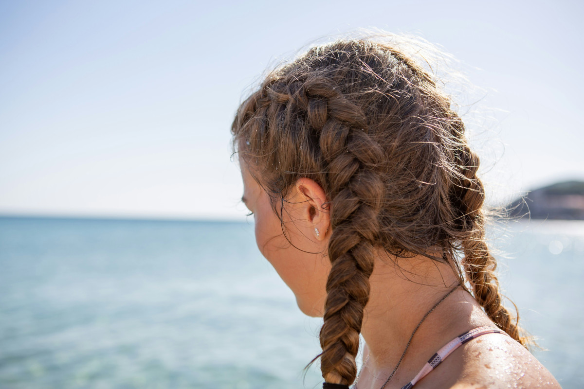 Ung kvinna sedd bakifrån med flätor på solig sandstrand